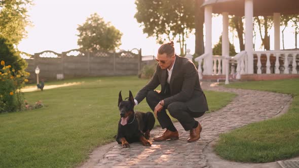 A Rich Businessman in a Business Suit Walks with a Big Doberman in the Park. A Successful Bearded