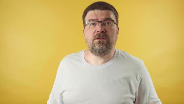 Angry caucasian middle-aged man in glasses with a beard screaming isolated  on yellow background.