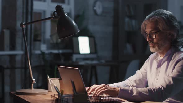 Man Typing On Laptop At Night Office