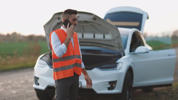 Young Man Use Smartphone Stading on Road Near the Broken Electric Car