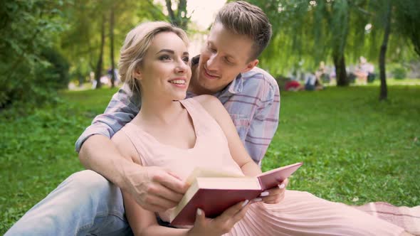 Couple in Love Sitting on Rug Reading Book Together, Gently Kissing in Breaks