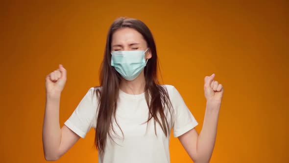 Woman in Medical Mask on Face is Very Happy and Claps Her Hands Against Yellow Background