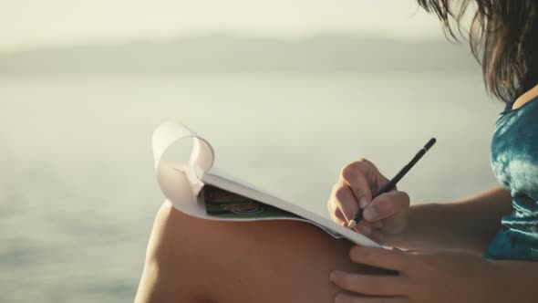 Closeup of Female Hands Drawing in Album with Pencil Picture By the Ocean