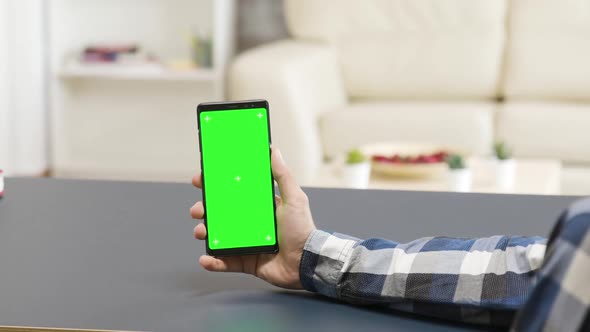 Zoom in Parallax Shot of Man Holding a Green Screen Phone on the Table