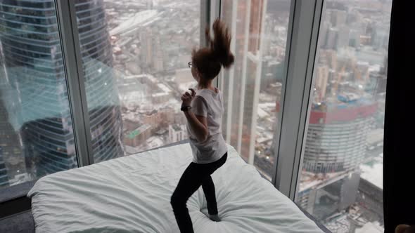 Cute Teenage Girl Jumping on the Bed Near the Window City View From Above