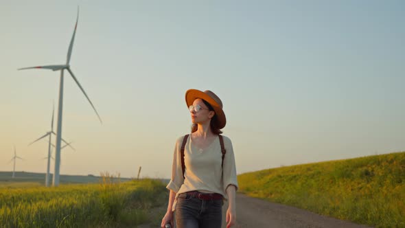 Young woman with retro camera walking next to windmill park farm at sunset