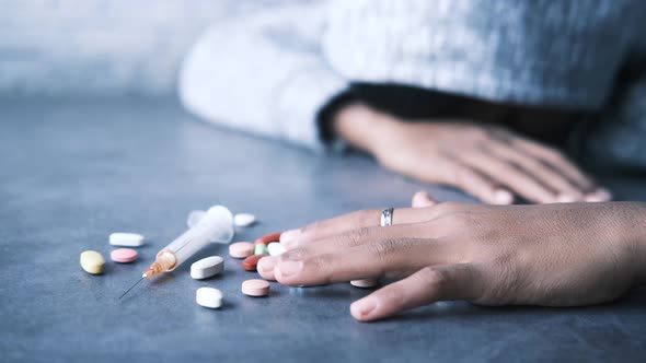 Drug Addiction Concept with Hand Holding Pills and Syringe Laying on Floor