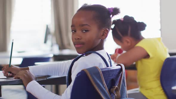 Portrait of happy african american schoolgirl sitting at classroom, making notes, looking at camera