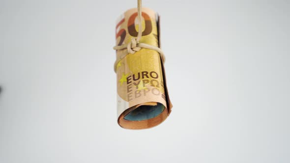 Roll of European cash banknotes tied with an elastic band swinging on a white background