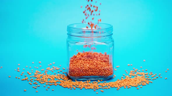 Closeup of Falling Down Red Lentils Into Glass Jar on Blue Background