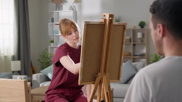 Young Woman Artist Draws a Portrait of a Man Using a Model