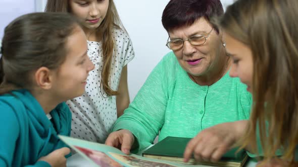 Closeup of Grandmother Showing Old Photo Album to Her Granddaughters