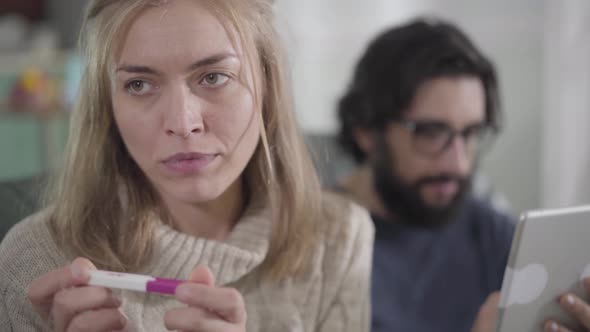 Close-up Portrait of Feared Caucasian Woman Looking at Affirmative Pregnancy Test As Her Husband