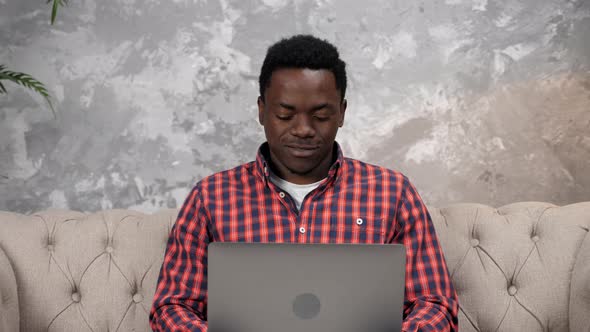 Smiling African American Man Sitting on Couch Work for Laptop Typing on Keyboard