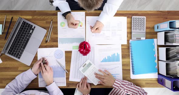 Business Team Throws Coins Into Piggy Bank at Workplace