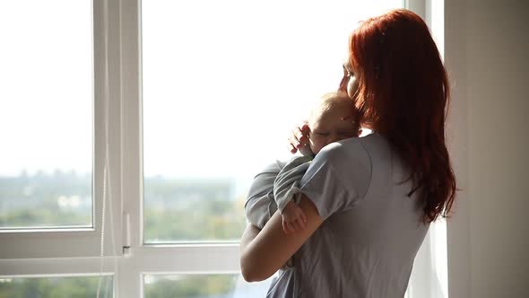 Ginger Woman Mother Holding Her Baby and Pats His Back and Looking in Window