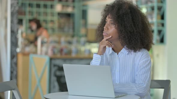 Pensive African Woman Thinking and Working on Laptop in Cafe 