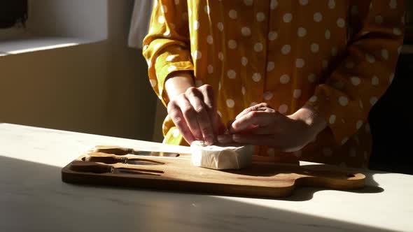 Female in yellow polka dot shirt with a cheese on table in kitchen