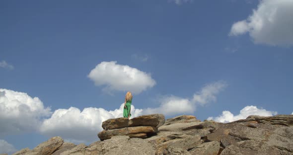 Young Pretty Woman in Green Dress is Dancing on a Rocky Hill on a Sunny Day