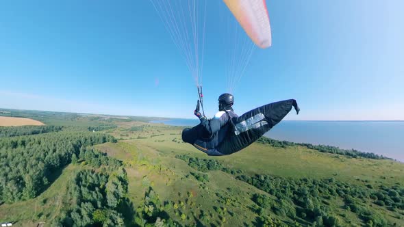 A Person Is Flying the Parawing Above the Green Fields