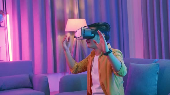 Asian Man Wearing Vr Headset At Living Room, Using Hand Touching And Slide, Cyan And Magenta Colors