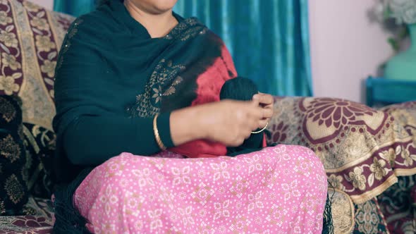 Traditional Indian woman roll the black thread into a ball and preparing it for knitting.