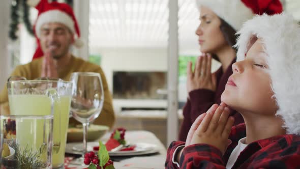 Focused caucasian son and parents praying together before christmas dinner