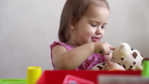 Small Toddler Girl Making Funny Expressive Grimace Face Playing with Soft Toy Bear at Home