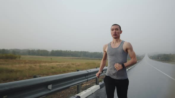 Athletic Man Runs Outdoor on Road in Steppe Doing Workout During Rain Front View