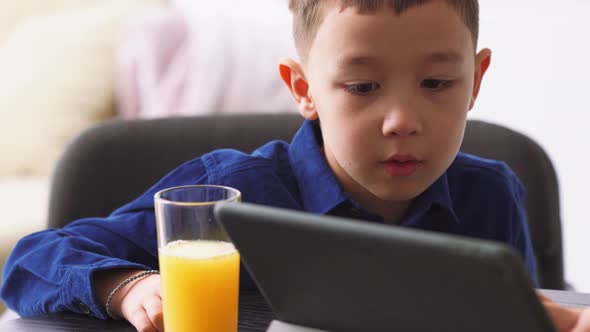 Pensive Asian little boy watching something on the tablet