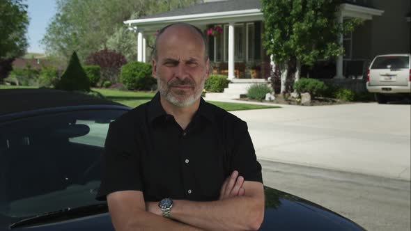 Static shot of a bearded man leaning on a car