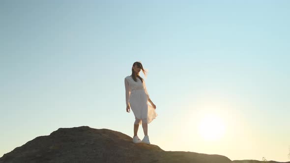 Beautiful Slender Woman in Translucent White Dress and White Sneakers Descending From Top of Hill
