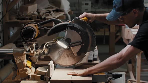 Carpentry Works Worker Puts Down a Big Circular Saw Over the Wooden Detail and Brings It to the