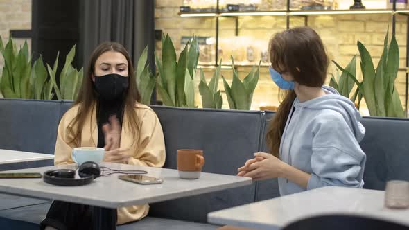 Two Young Beautiful Women in Covid Face Masks Sitting in Cafe and Chatting