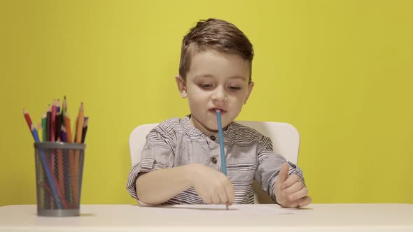 Smiling little boy at the table draw with crayons for mum on yellow background. Creativity concept