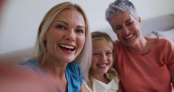 Caucasian grandmother, mother and daughter waving while having a videocall on smartphone at home