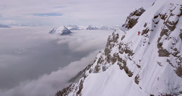 Aerial drone view of a skier skiing down a steep snow covered mountain