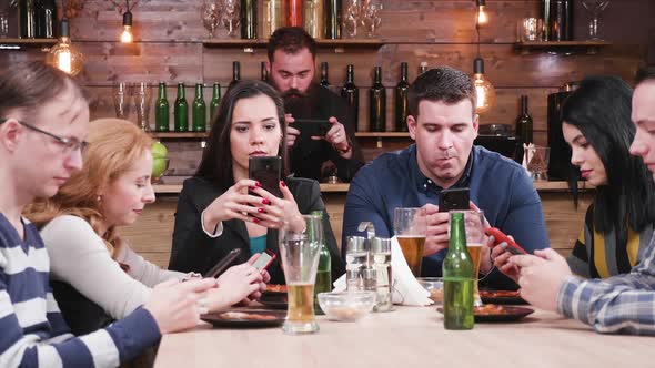 Friends in a Pub All Look at Their Smartphones