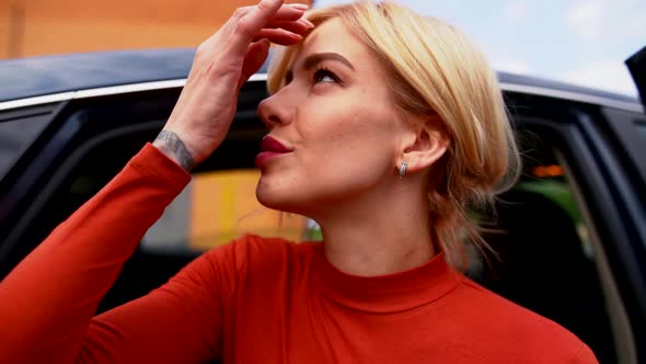 Blonde Carefree Woman Is Sitting at Car with Open Door and Looking Outdoors