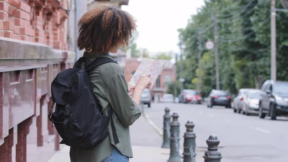 Young African American Girl Tourist with Backpack Traveling in Big City Alone Holding Paper Map in