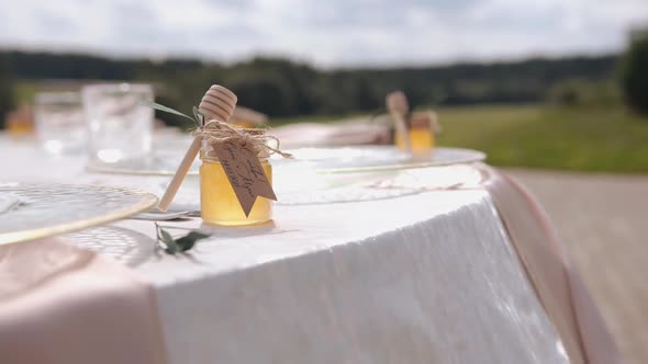 Decorated Outdoors Table with Glassware and Small Honey Jars with Wooden Honey Dippers for Wedding