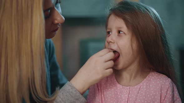 Smiling Mother Puts Pill Onto Tongue of Little Daughter