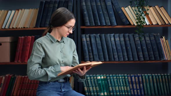 Confident Brunette Woman Reading Vintage Paper Book Turning Pages at Public Home Library Interior alt