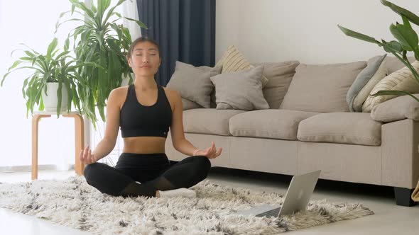 Calm asian lady, dressed in sportswear, meditates on floor in room