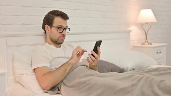 Young Man Using Smartphone in Bed