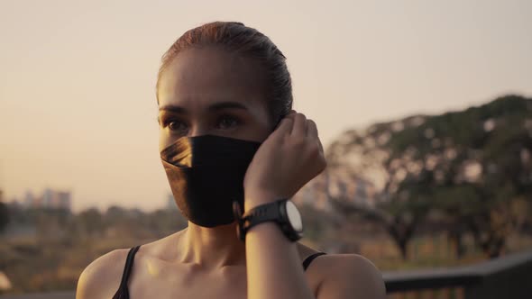 Woman in sportswear wearing a protective mask and putting wireless earphones before start jogging.