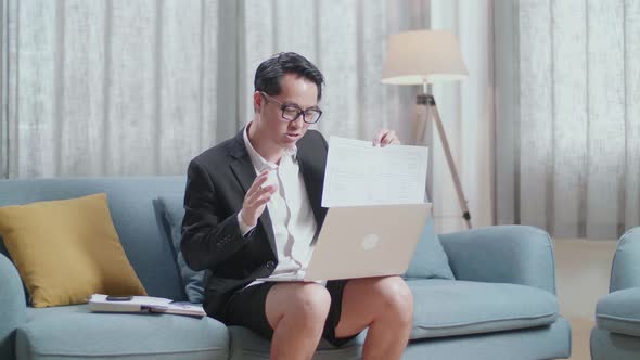 Asian Businessman In Jacket And Shorts Presenting Work Paper On A Laptop At Home