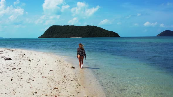 Young Caucasian woman walking alone on exotic beach washed by calm clear water of shallow lagoon at