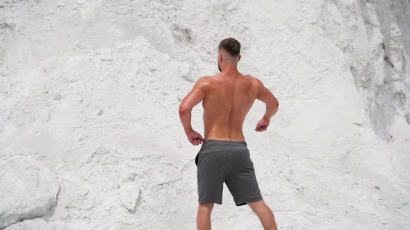 Backside view of a bodybuilder outdoors. Strong athlete without shirt shows his muscular body