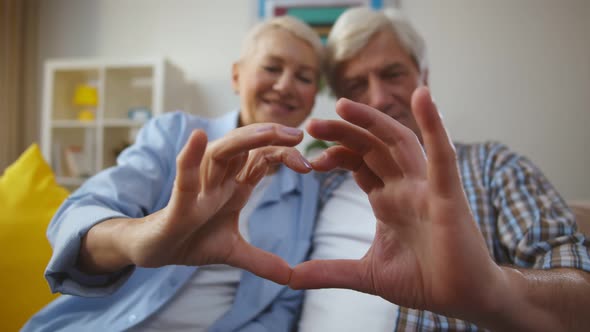 Cheerful Senior Couple Making Heart Shape with Their Hands and Fingers at Home